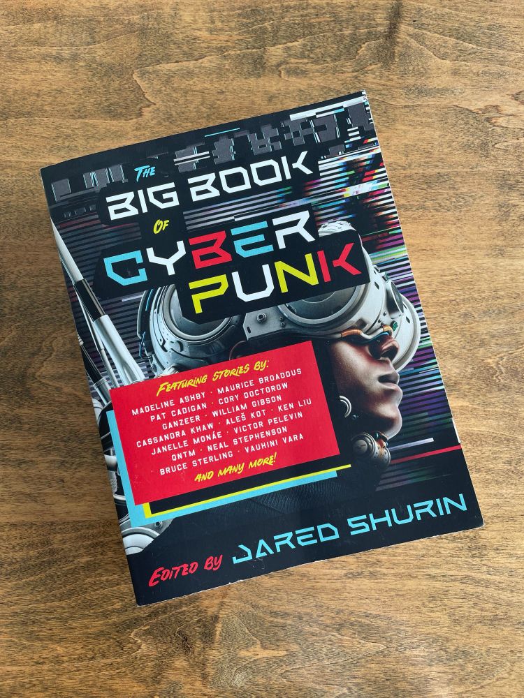Thick trade paperback book with bold colors and “Big Book of Cyberpunk” in futuristic font across the front. 