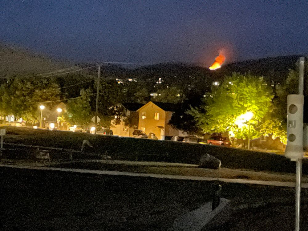 Wildfire lights up night sky and mountainside near Missoula, Montana, with houses in the foreground. 