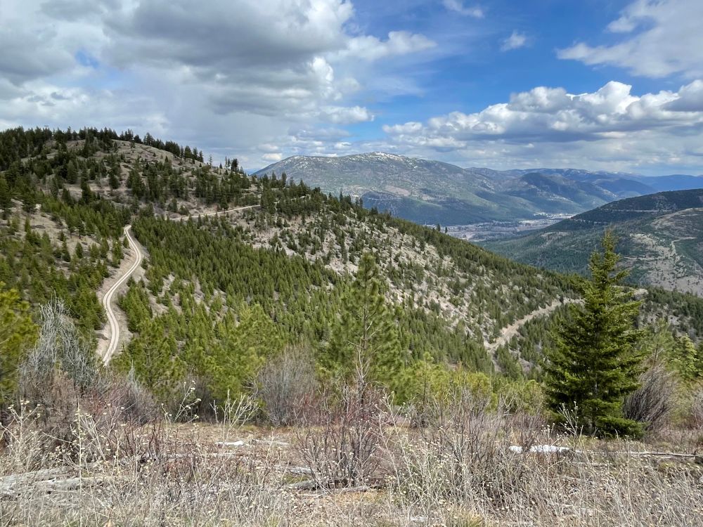 Looking down on rolling mountains and a gravel road winding its way up their sides. 