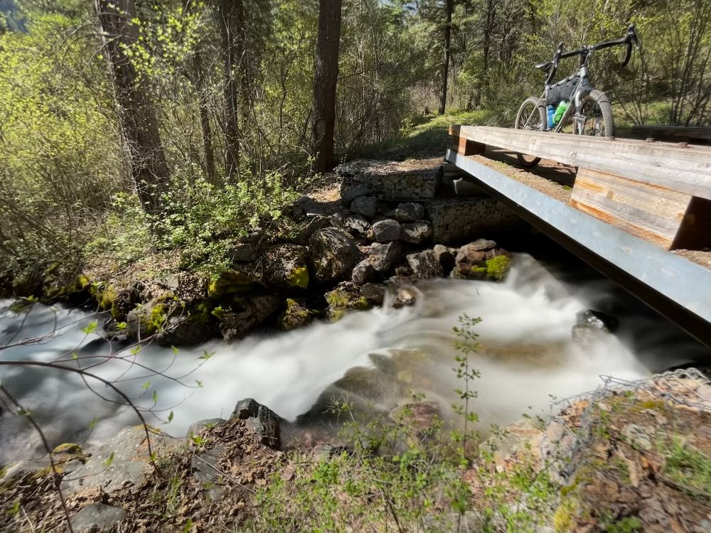 Waterfall flowing under a bridge with a Kona Rove bicycle leaned against the top