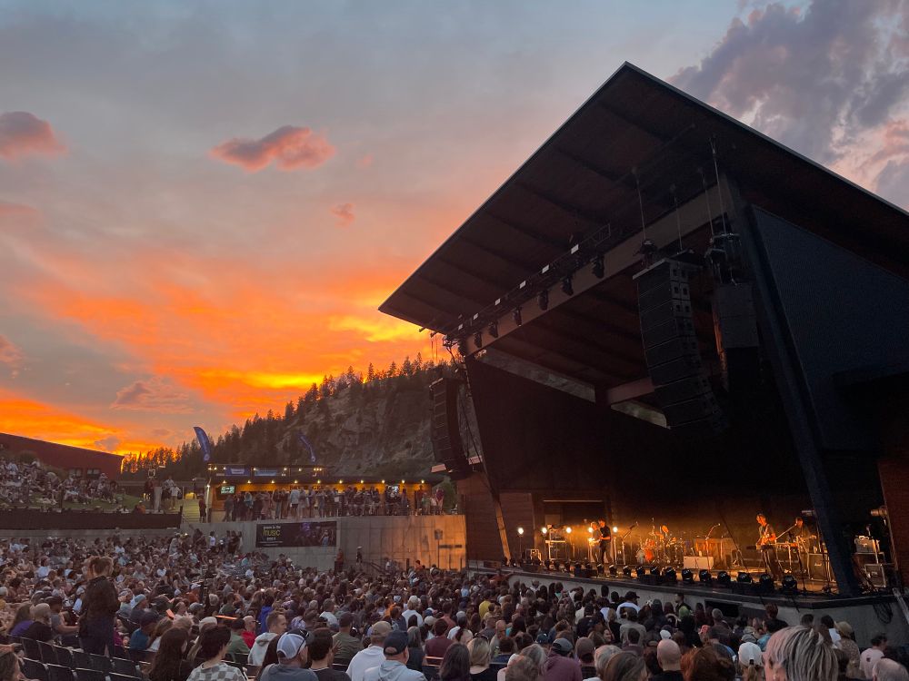 Kettlehouse Amphitheater stage opening to a crowd of adoring fans watching the indie band death cab for cutie and orange sunset against the clouds in the background. 