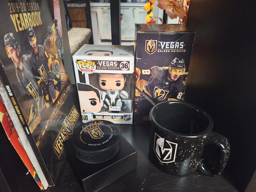 A picture of memorabilia of Las Vegas Golden Knights hockey team, including an autographed puck from William Karlsson, a Funko pop figure of Marc-André Fleury, magazines, and a coffee mug with the team's logo