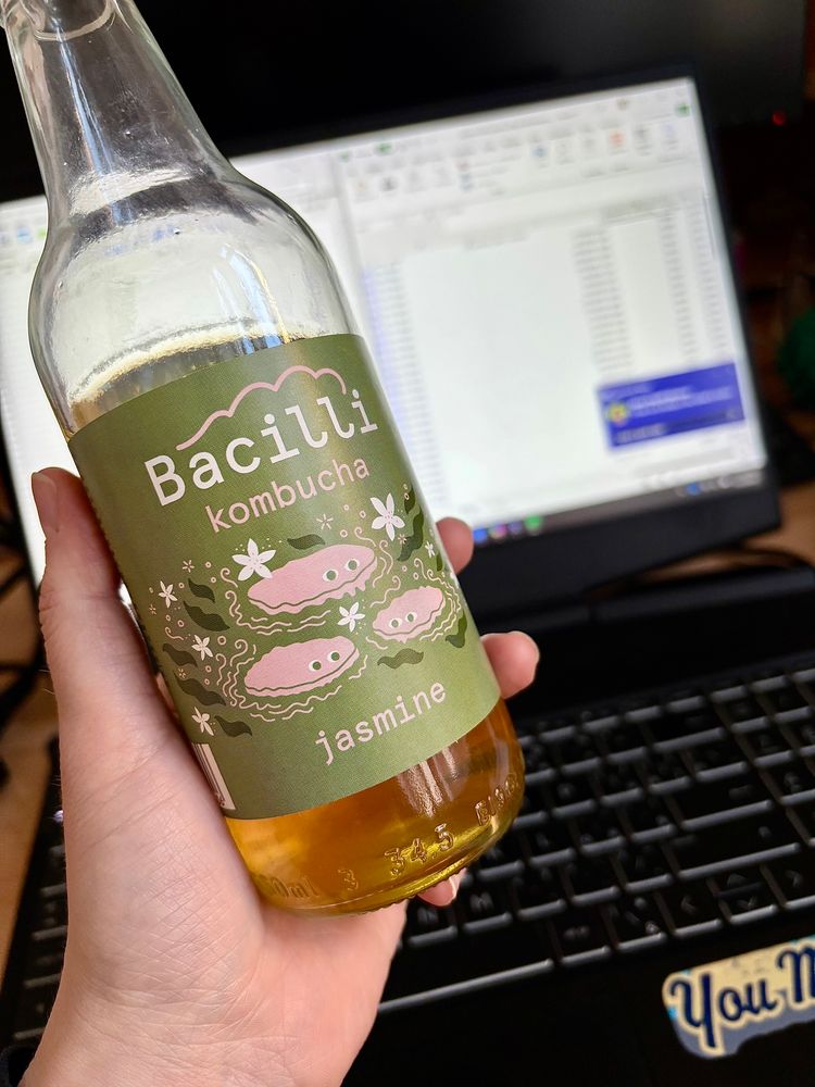 A jasmine kombucha glass bottle in front of a laptop with data on the screen.