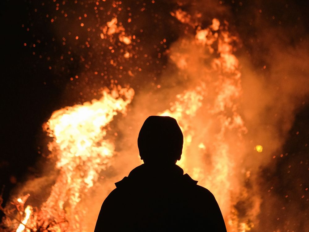 Photo of a man in silhouette looking at an enormous fire in front of him