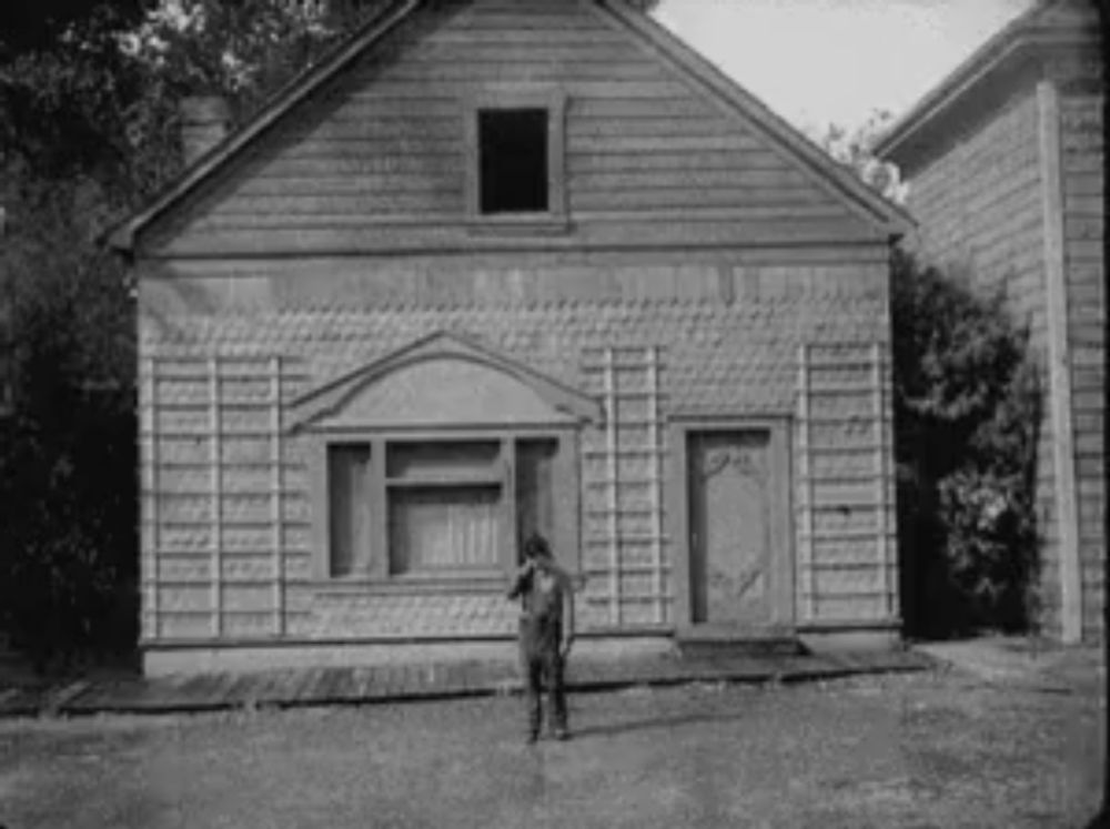 a man is standing in front of a house in a black and white photo .