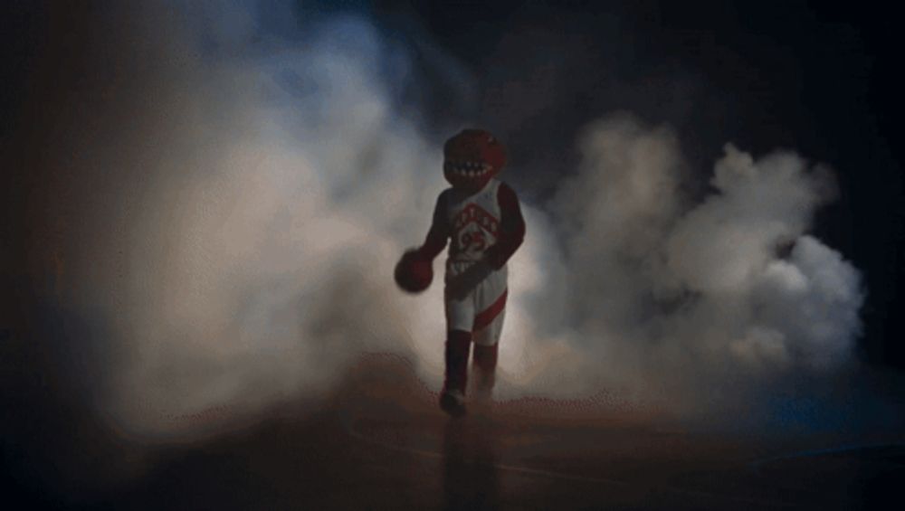 a toronto raptors mascot holding a basketball in the dark