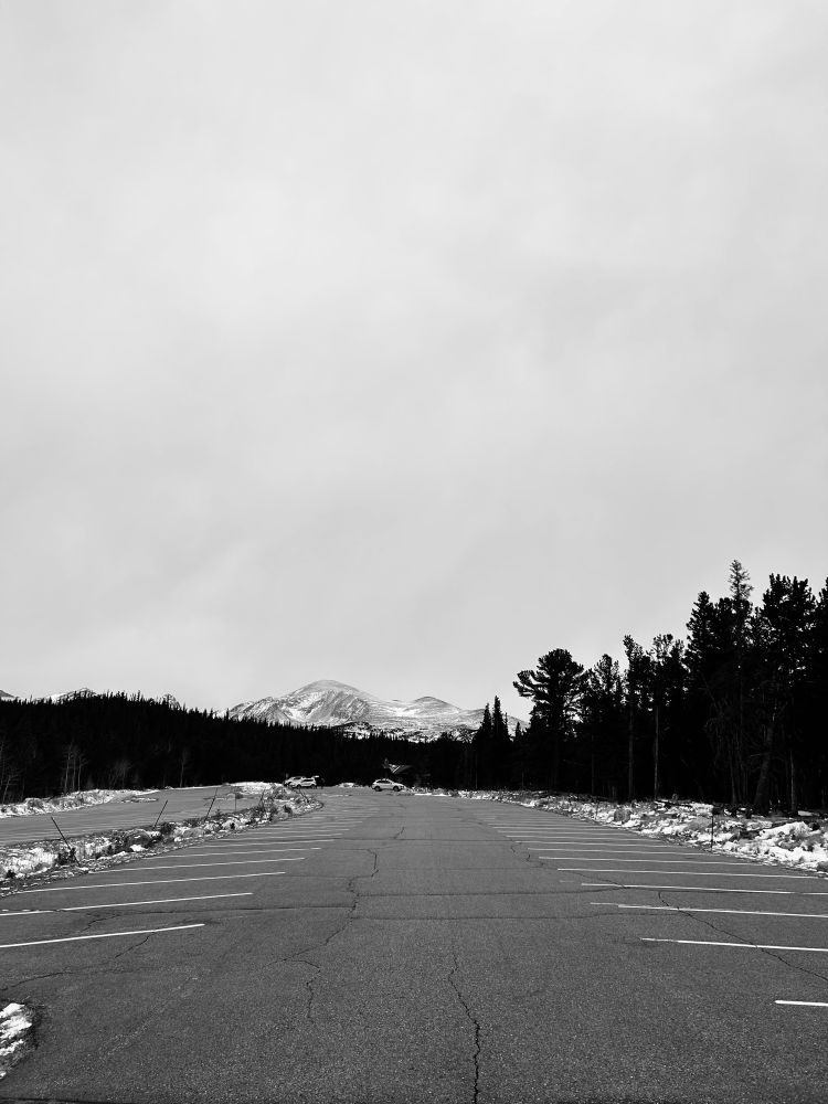 An empty parking lot surrounded by the forest with the peak of Mt Audubon in the distance