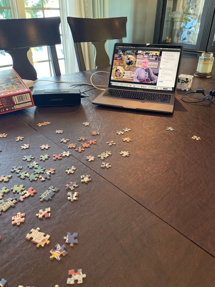 Steven Page on a zoom meeting playing guitar. Puzzle pieces spread out on a dining room table.