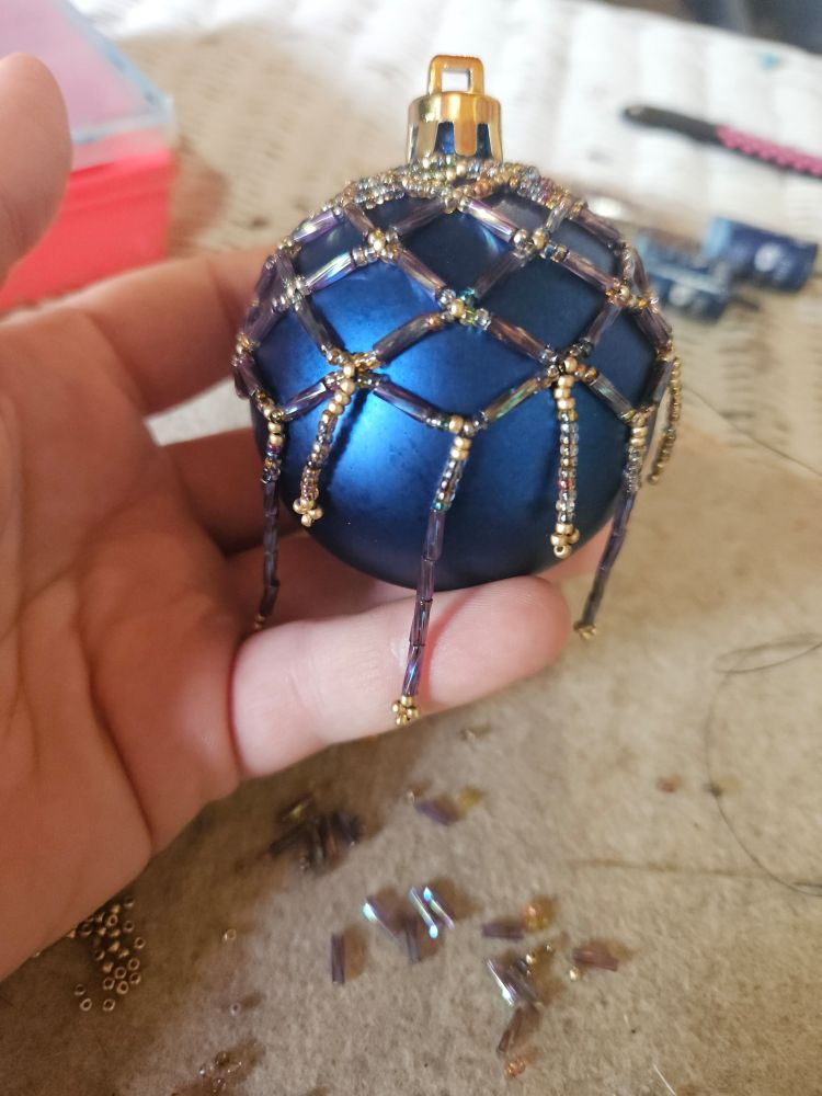 A beaded ornament, dark blue, with a beaded netting of purples and copper
