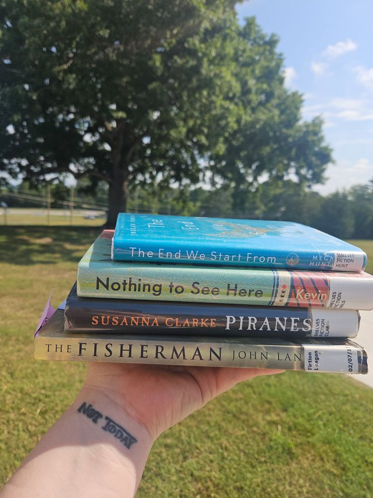 A stack of books in front of a large oak tree. Top to bottom: The End we Start From, Nothing to See Here, Piranesi, and The Fisherman. 