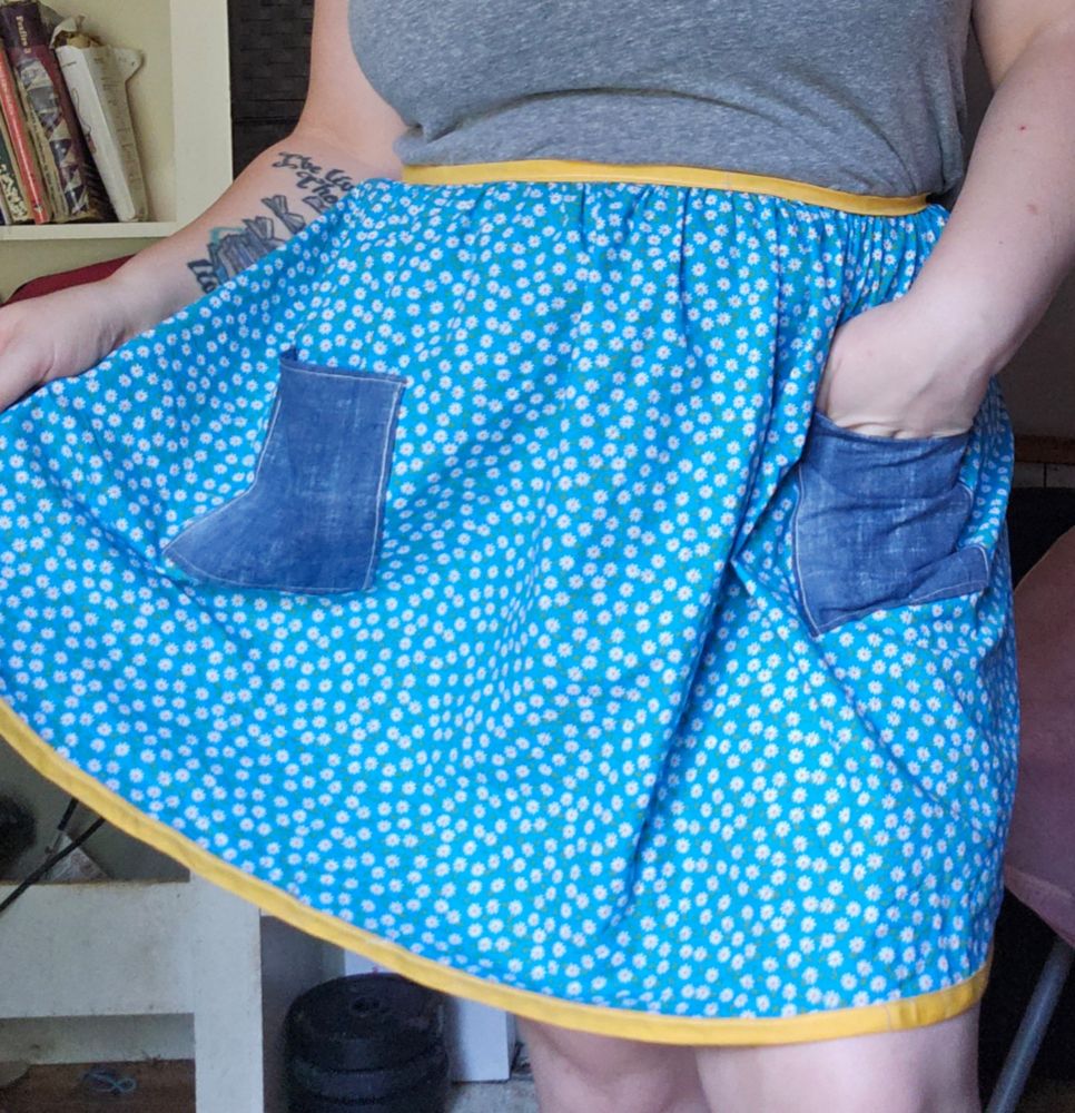 A floral apron of tiny flowers on a blue background with yellow trim and denim pockets. 