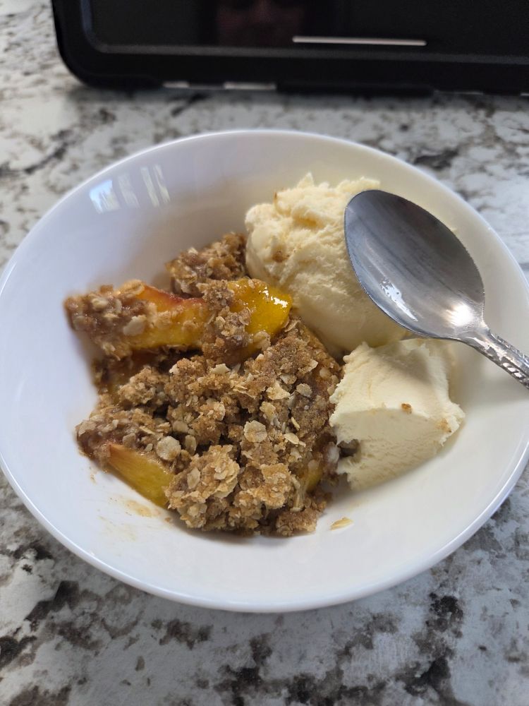 Peach crisp with vanilla ice cream in a white bowl with a spoon