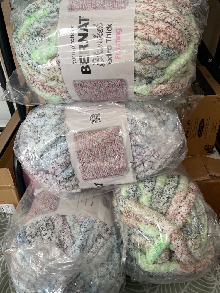 Showing a pile of Bernat Bulky Extra Thick Frosting yarn. This yarn is very plush with speckles of purple, blue, green, black and light brown. 