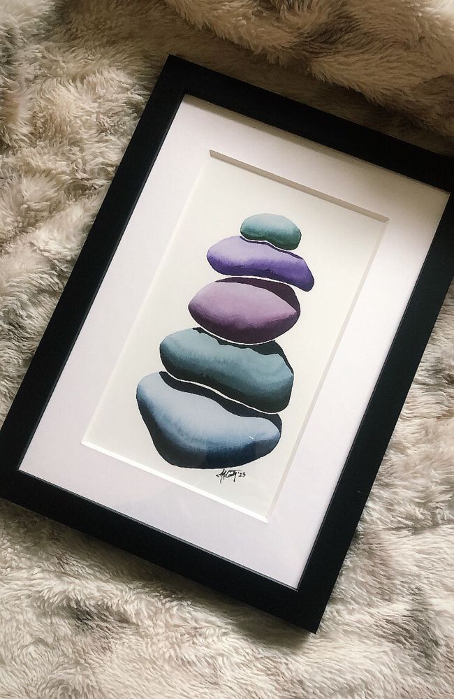 An art print of a rock cairn (rock stack) coloured in deep blues, greens and purples. 

The frame of the print is black and the background is a soft white/grey and fur texture. 