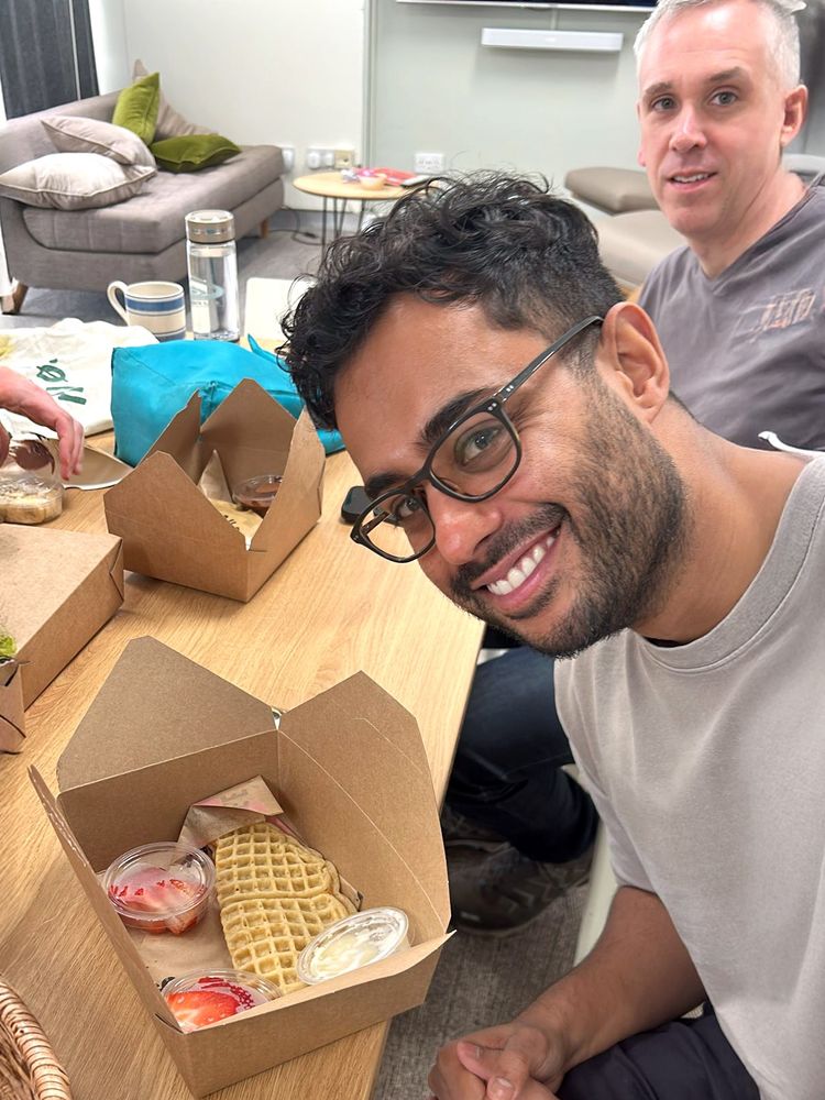 Two men who work at Nile are smiling at a box of waffles. The waffles come with strawberries and cream.