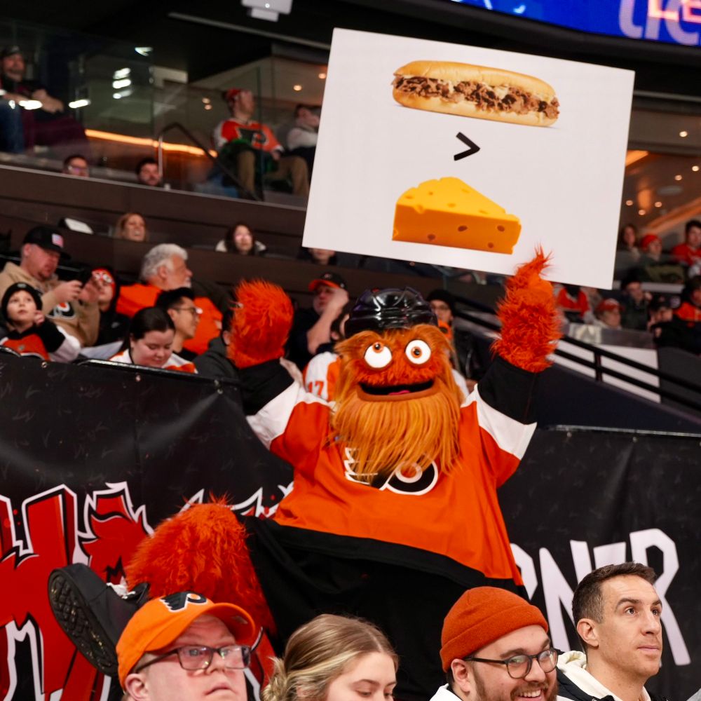 Gritty holding a sign that says the Philly Cheesesteak is better than cheddar 
