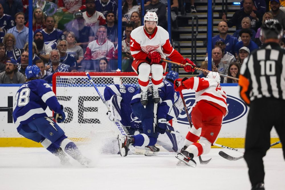 Red wings player floating in the air while a teammate is shooting the puck.