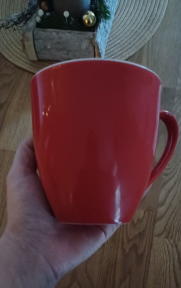 Eine linke Hand hält eine überdimensioniert große Tasse, die viel größer ist als alle Hände dieser Welt.