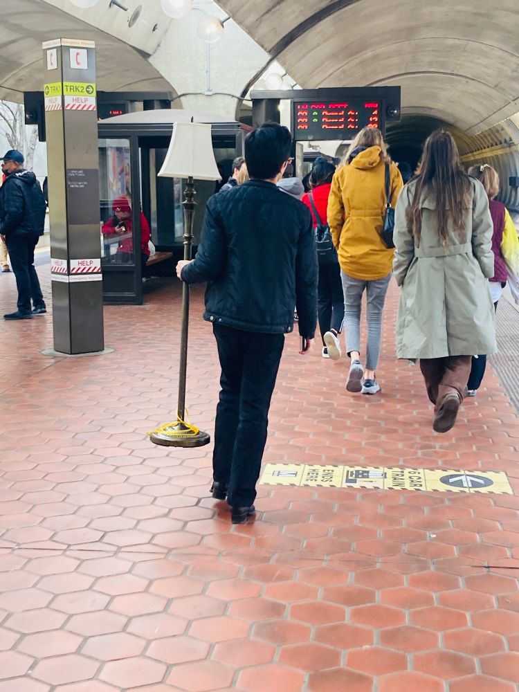 A metro rider carries a floor lamp. 