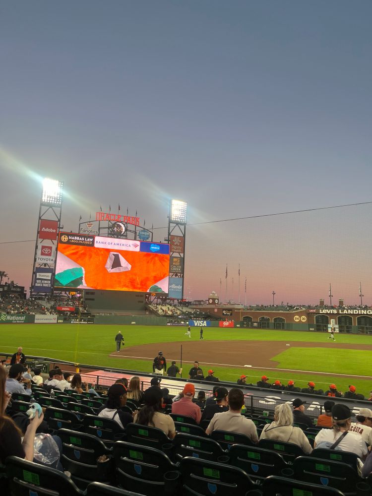 A picture of Oracle park’s (a baseball stadium in San Francisco) jumbotron at sunset from behind the dugout.