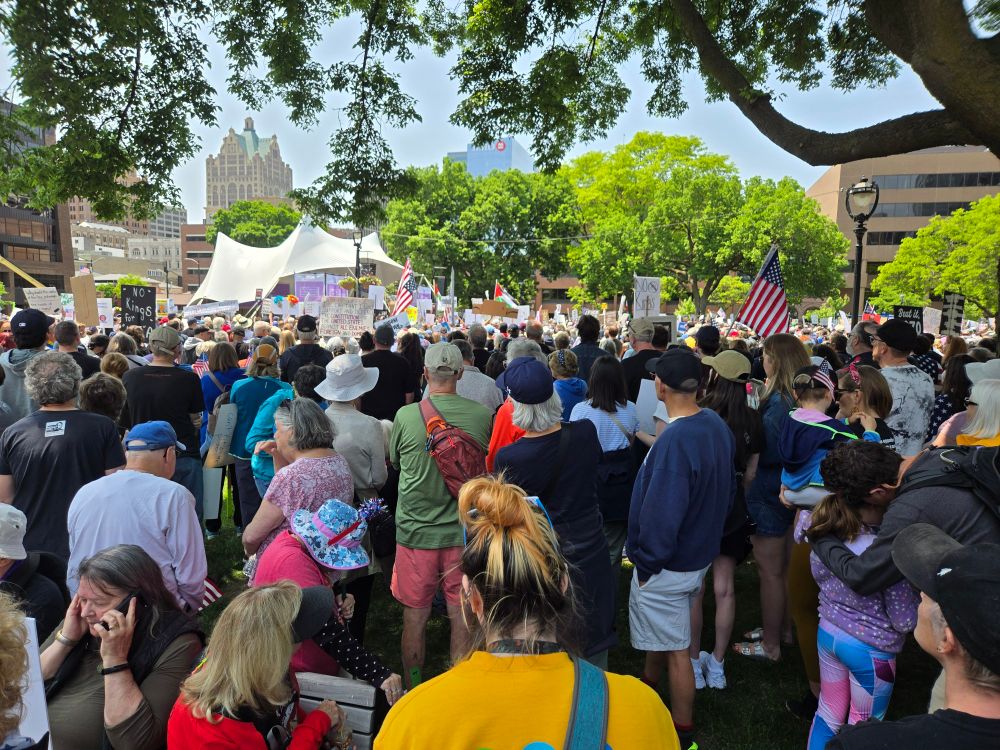 View of the bandshell in Cathedral Square, Milwaukee Wisconsin, in the background with #NoKings protesters filling the park in the foreground.