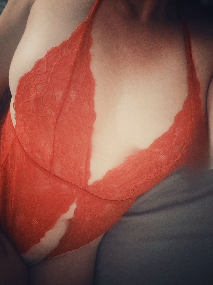 Photo couleur du buste d’une superbe femme allongée en body de dentelle rouge. Très pratique puisque déjà ouvert en bas…