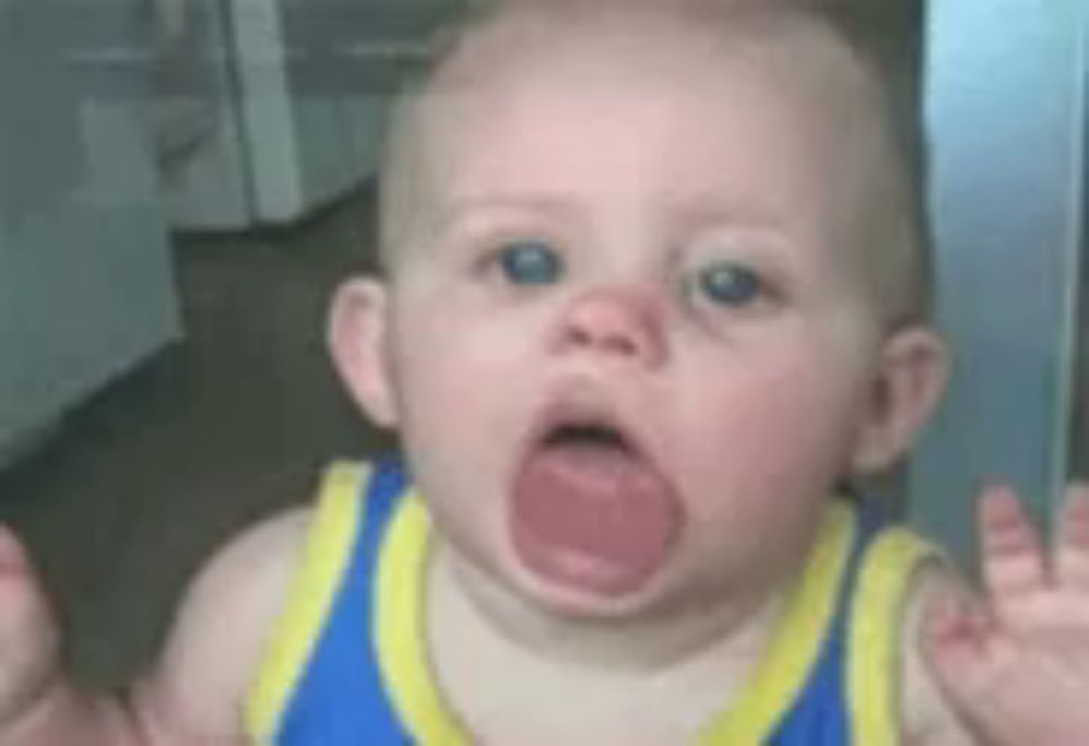 a baby is making a funny face with his mouth open .