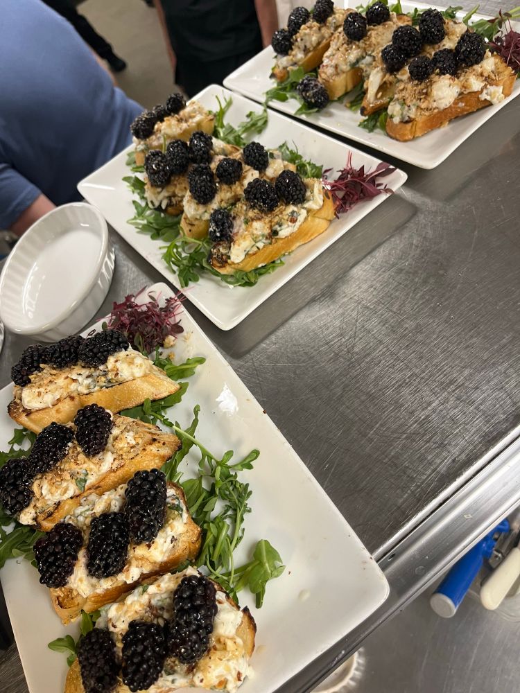 Bruschetta with cheese, basil, blackberries, and honey on a bed of arugula on a white plate