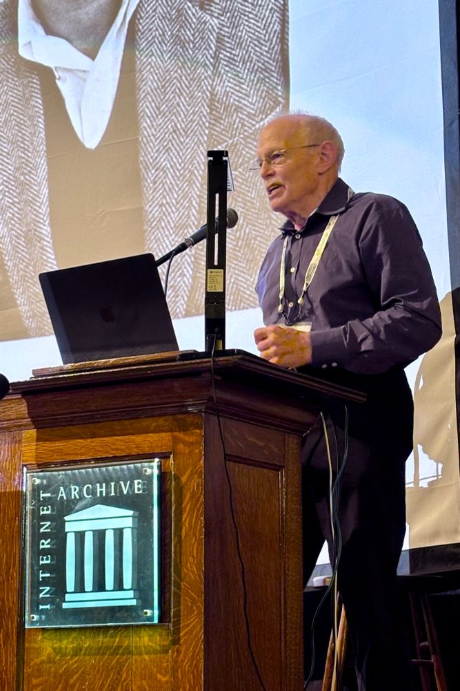 Jay McClelland stands behind a wooden lectern with an “Internet Archive” logo, speaking into a microphone.