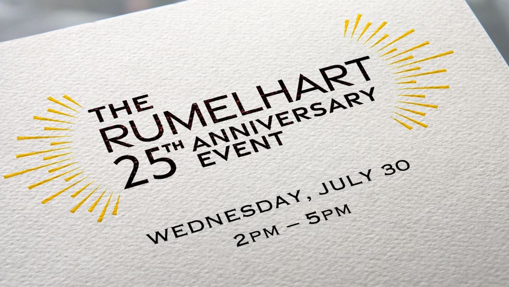 Close-up of an elegant invitation card with embossed and metallic lettering. The text reads: 'THE RUMELHART 25TH ANNIVERSARY EVENT' with decorative golden sunburst designs on either side. Below, the date 'WEDNESDAY, JULY 30' and the time '2PM – 5PM' are printed in black ink on textured white cardstock.