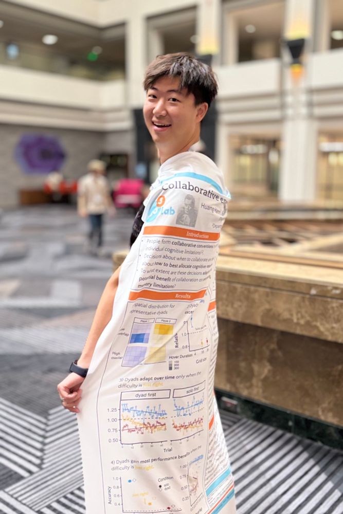 A smiling researcher at CogSci 2025 stands indoors wearing their scientific poster draped like a cape, with charts, graphs, and text visible on the fabric. The background shows a spacious conference hall with people walking and blurred architectural details.