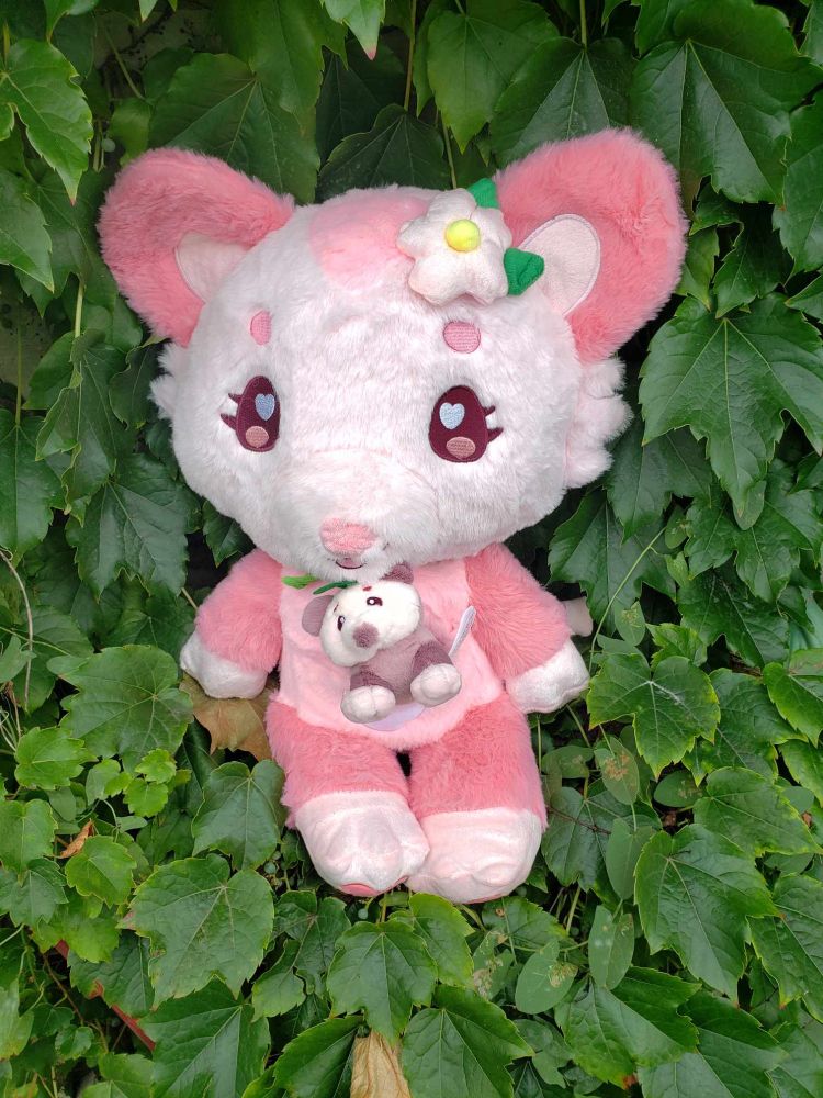 An adorable pink possum stuffed animal, with a flower by her ear, and a tinier baby possom stuffed animal inside her tummy pocket. They are posing among ivy leaves.