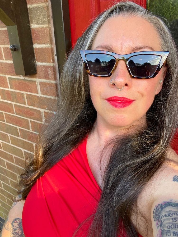 Selfie of KP with sunglasses on, makeup; notably red lips, a one shoulder red dress, and her hair down 