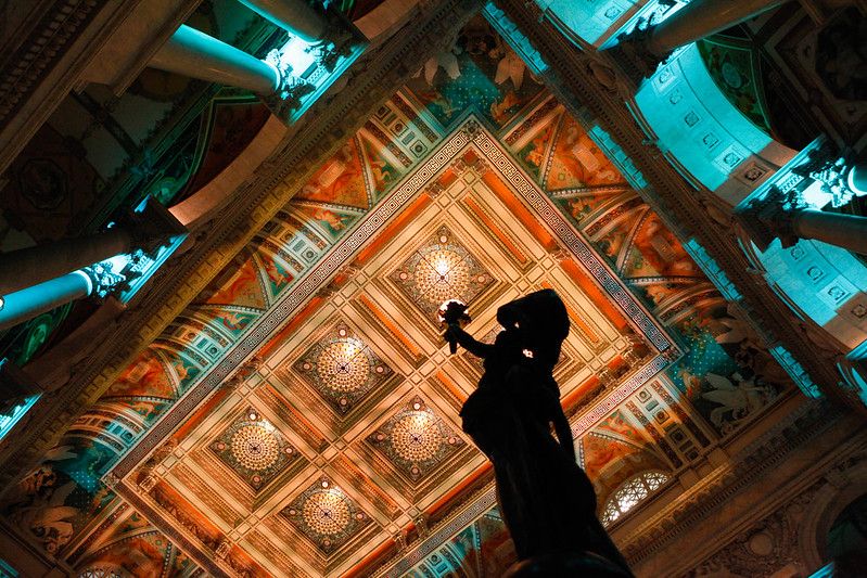 The ceiling of the Library of Congress Jefferson Building's Great Hall is lit up during an event on September 9, 2015. The point of view is from below a statue holding a torch toward the ceiling, which is decorated with intricate geometric patterns. Photo by Shawn Miller/Library of Congress.