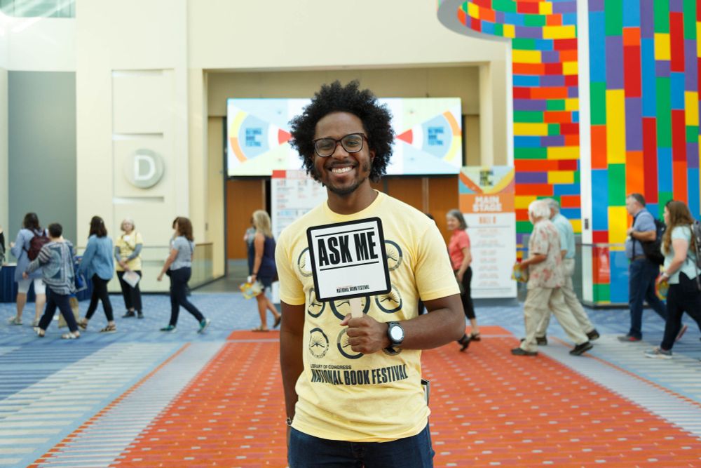 Volunteer Solomon Scott smiles as he holds an "Ask Me" sign while working the morning shift of the National Book Festival outside the Main Stage, August 31, 2019. Photo by Shawn Miller/Library of Congress.

