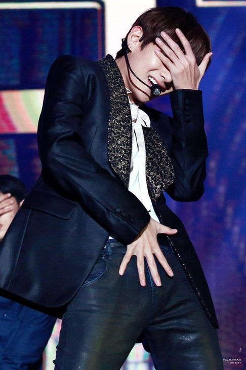 A photo of Kim Taehyung during a performance. He's covering his eyes with one hand and his other hand is pressed to the front of his leather pants. 