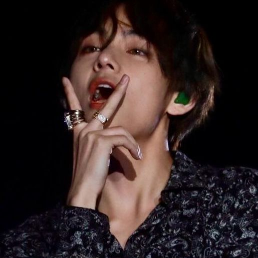 A photo of Kim Taehyung making a “V” sign with his fingers in front of his open mouth. 