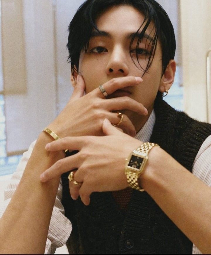 A photo of Kim Taehyung from his FRI(END)S performance. He is touching the bottom half of his face, with his fingers against his lips, wearing gold jewelry. 
