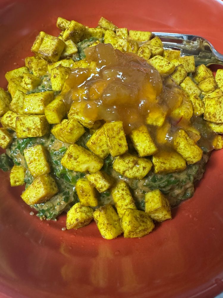 A bowl of vegan palak paneer, topped with baked tofu and mango chutney
