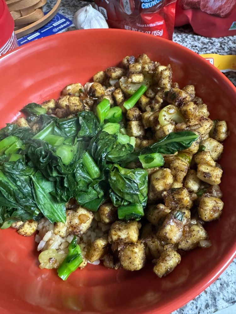 A bowl with fried tofu, chopped gai lan leaves and stems, and rice