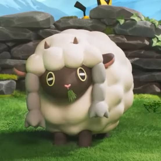 A picture of the Pokemon Wooloo eating grass in front of a wall. There’s a Pichu obscured by the wall in the background.