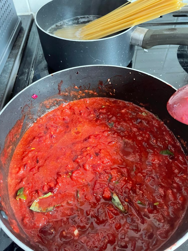 A homemade tomato sauce with basil and sage, and a separate saucepan of boiling spaghetti.
