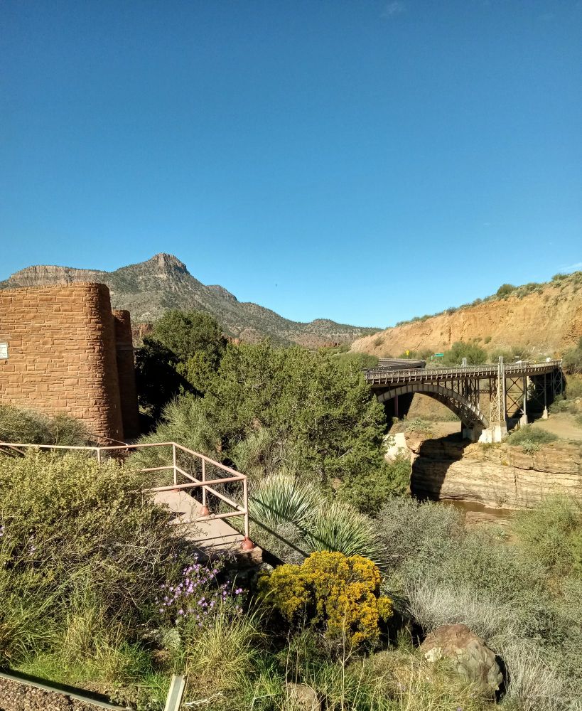 A desert canyon, with bridges crossing a river and high desert shrubbery in the foreground 