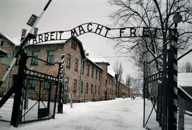 A photo of a wintery Auswitch and the famous gate with the text: ARBEIT MACHT FREI.