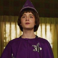 Will Byers from stranger things wearing a purple robe and wizard hat with silver stars on it.