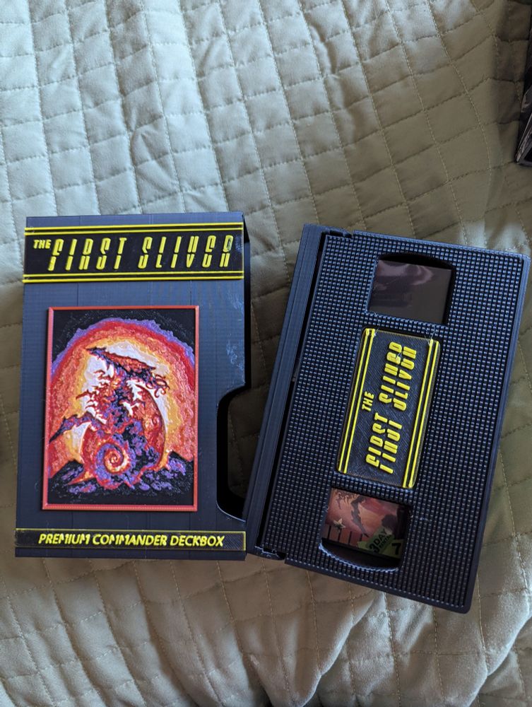 3D printed magic the gathering commander deck box modeled to look like an old slip case and VHS for a horror movie. On the tap and slip case it reads "The First Sliver" with an image like the original Alien movie poster.