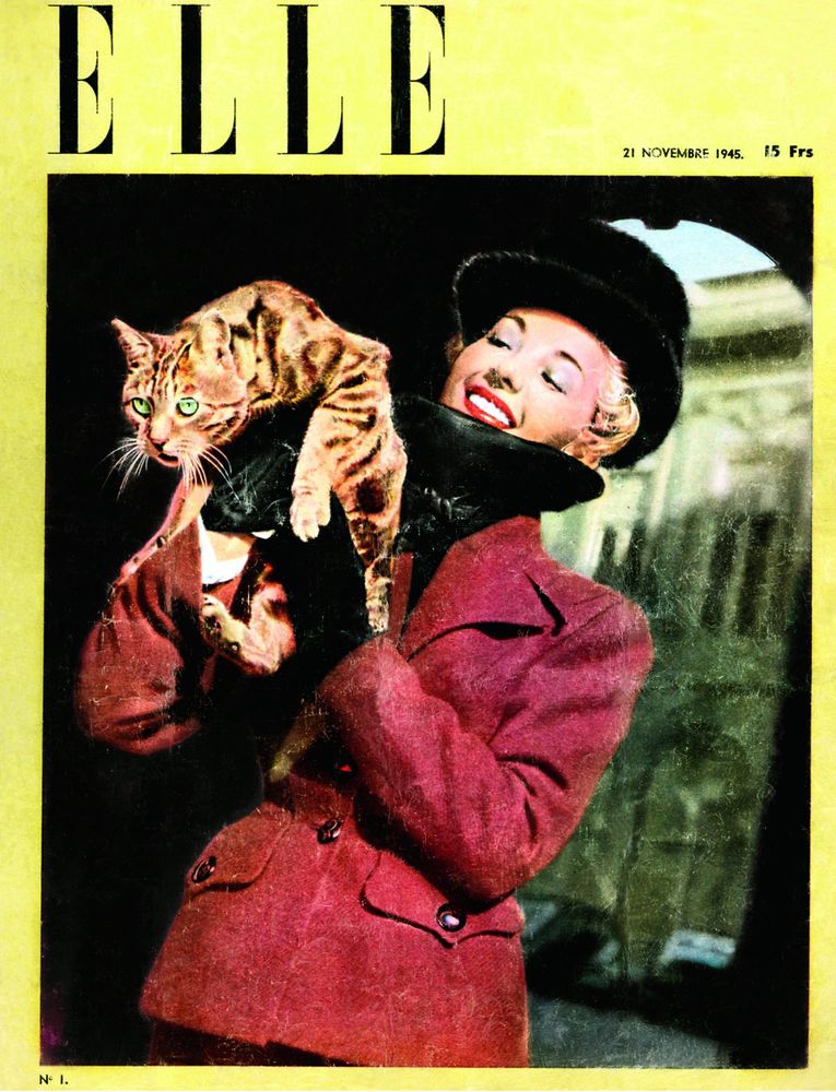 Portada del primer número de la revista ELLE. 21 novembre 1945, 15 Frs. (Francs). S'hi veu una dona amb barret negre i jaqueta vermella. Té a les mans un gat que fa tota la cara de voler fugir d'allà.