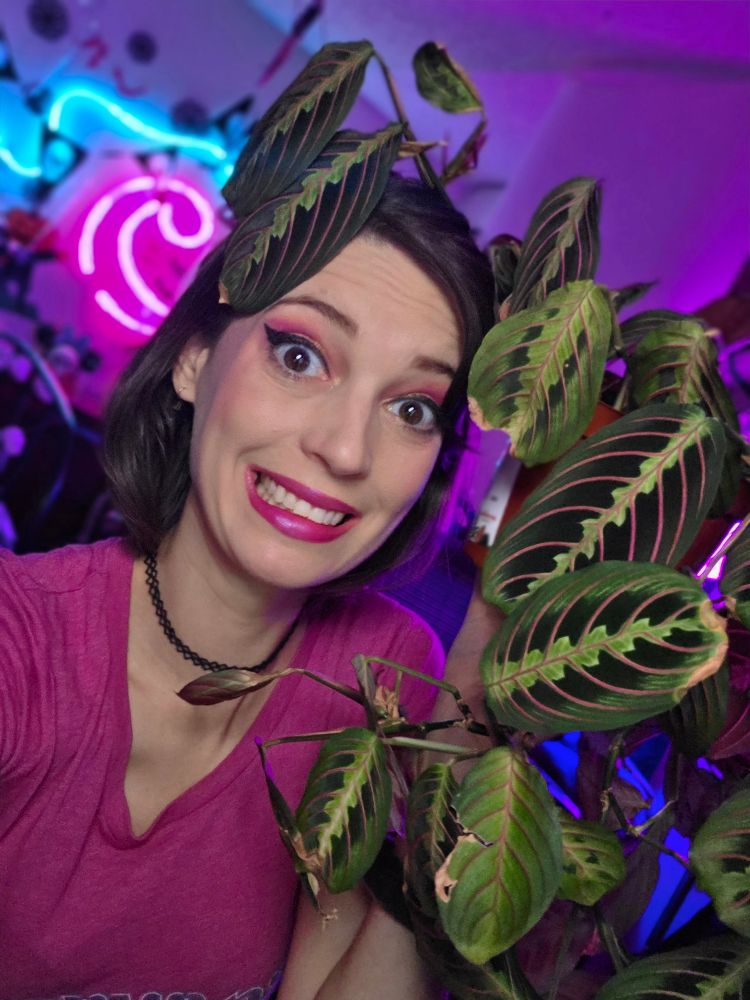 Char smiling nervously holding a red prayer plant draped on her head. .