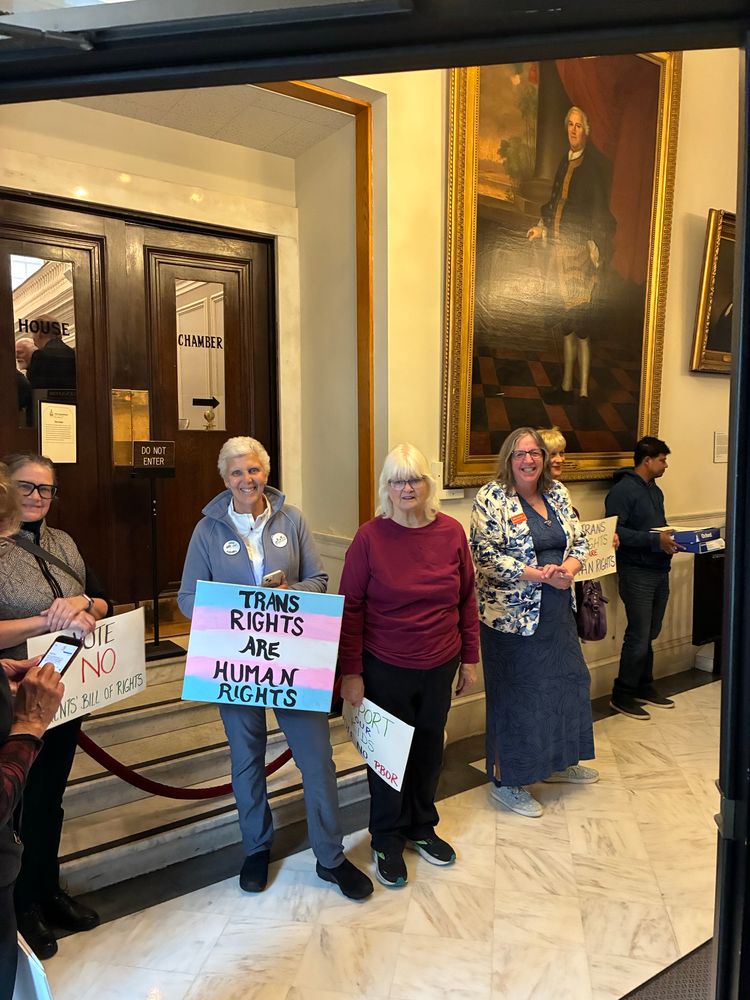 Several people in the State House hallway; most prominent sign says "Trans rights are human rights"
