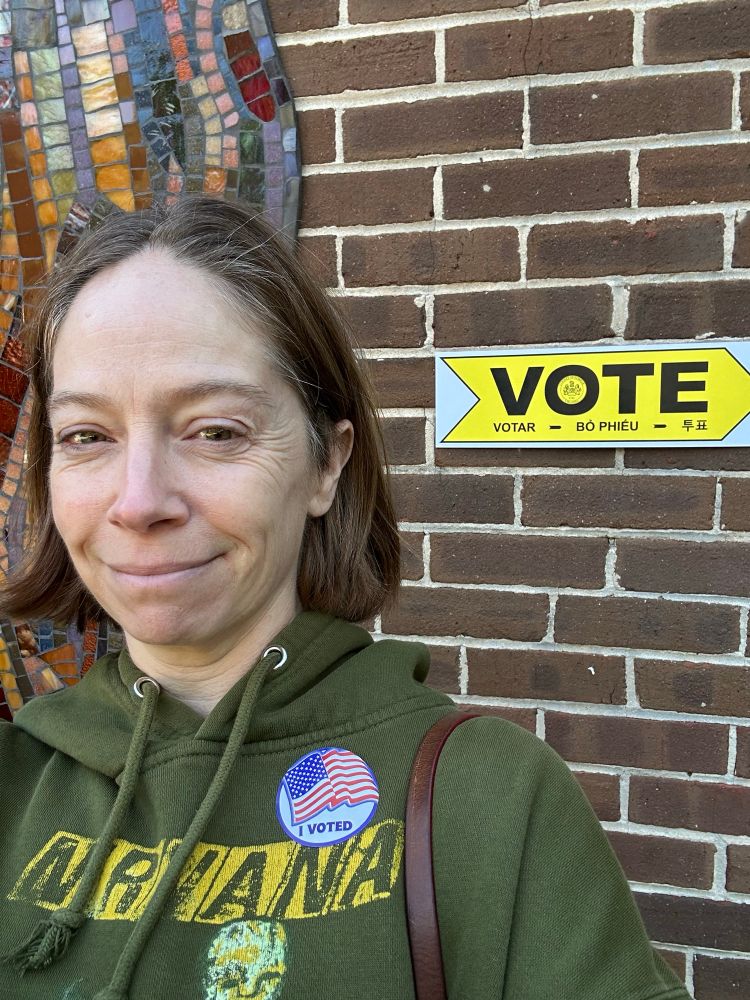 Photo of me with I Voted sticker under Vote Here sign